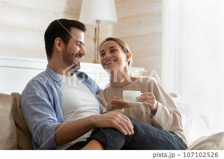Smiling woman drinking hot beverage, sitting on loving husband laps Smiling woman drinking hot beverage, sitting on loving husband laps 107102526