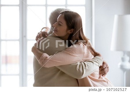 Loving grownup daughter and old dad hugging at home Loving grownup daughter and old dad hugging at home 107102527