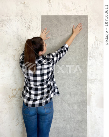 Brunette woman trying out new wallpaper at home a newly painted white wall for visual effect 107103611