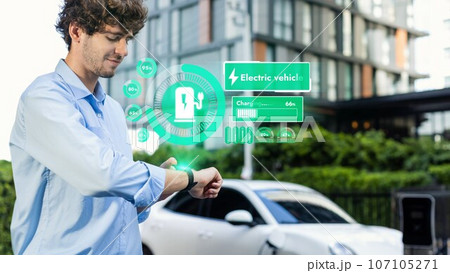Businessman checking EV car battery status in hologram from smartwactch. Peruse Businessman checking EV car battery status in hologram from smartwactch. Peruse 107105271