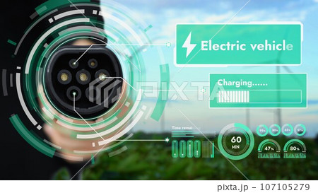 EV charger pointing in front of camera with blurry wind turbine farm. Peruse EV charger pointing in front of camera with blurry wind turbine farm. Peruse 107105279