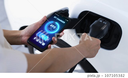 Hand insert EV charger and check battery status hologram from smartphone. Peruse 107105382