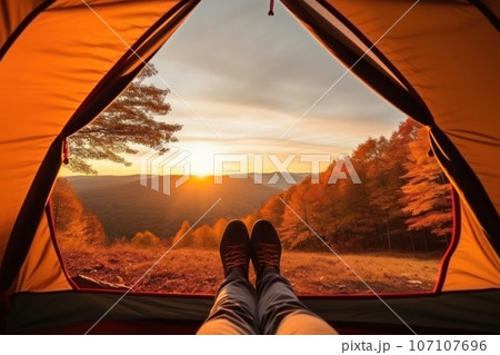 A man enjoys the view of the autumn mountains while lying in a tent. 107107696
