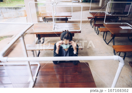 Woman having headache while sitting on wooden table in canteen and wearing mask for protect virus disease in covid-19 pandemic. 107108302