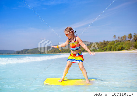 Child surfing on tropical beach. Surfer in ocean. 107110517