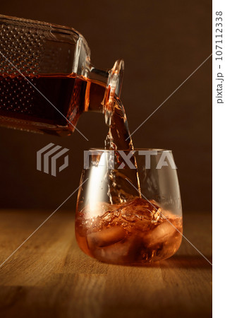 Whiskey is poured into a dammed glass with ice. Whiskey is poured into a dammed glass with ice. 107112338