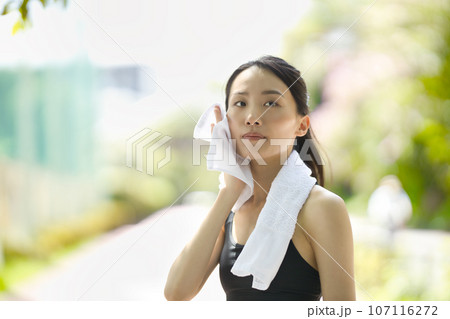 緑の中タオルで汗を拭くスポーツウェアの若い女性 107116272