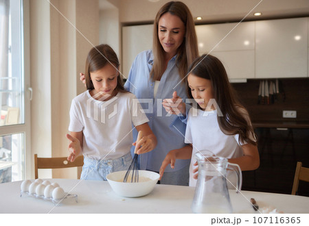 Cute little girl and her beautiful mom in aprons are playing and laughing while kneading the dough in the kitchen. Cute little girl and her beautiful mom in aprons are playing and laughing while kneading the dough in the kitchen. 107116365