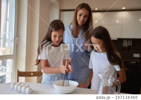 Cute little girl and her beautiful mom in aprons are playing and laughing while kneading the dough in the kitchen. Cute little girl and her beautiful mom in aprons are playing and laughing while kneading the dough in the kitchen. 107116368