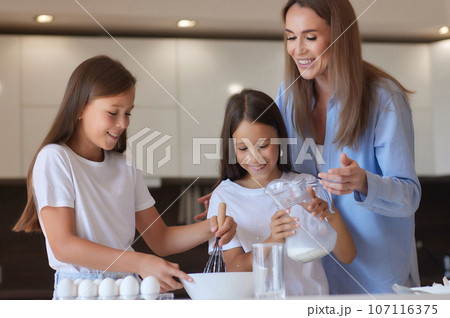 Cute little girl and her beautiful mom in aprons are playing and laughing while kneading the dough in the kitchen. Cute little girl and her beautiful mom in aprons are playing and laughing while kneading the dough in the kitchen. 107116375