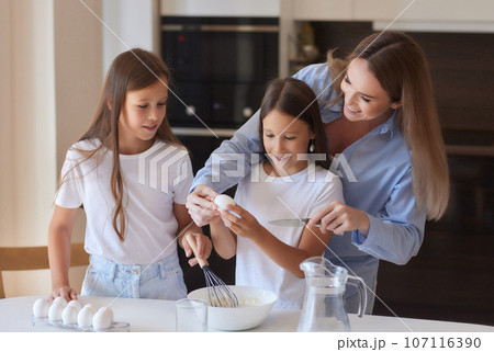 Cute little girl and her beautiful mom in aprons are playing and laughing while kneading the dough in the kitchen. Cute little girl and her beautiful mom in aprons are playing and laughing while kneading the dough in the kitchen. 107116390