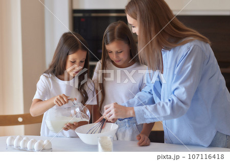Cute little girl and her beautiful mom in aprons are playing and laughing while kneading the dough in the kitchen. Cute little girl and her beautiful mom in aprons are playing and laughing while kneading the dough in the kitchen. 107116418