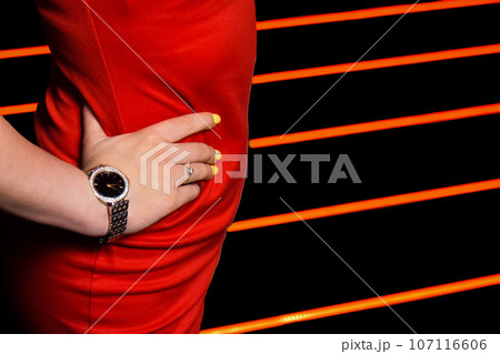 The hand of a person with a hand watch poses on the waist in a red dress, an element of a part of a woman's figure on a striped background 107116606