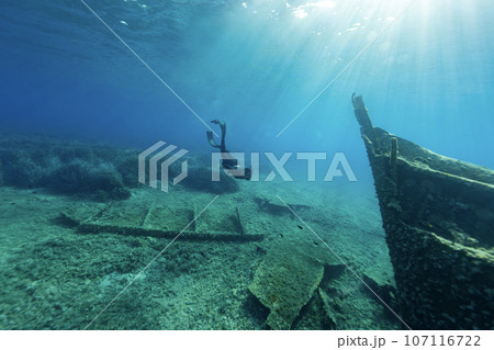 Freediver diving towards a shipwreck at the bottom of the sea. Young man dIver eploring sea life. 107116722