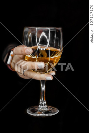 A woman's hand holds out or holds a glass of alcoholic beverage from the darkness close up 107117176