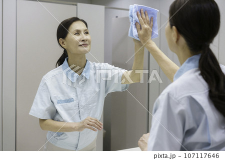 オフィスの洗面所で鏡を拭くシニア女性清掃員 107117646