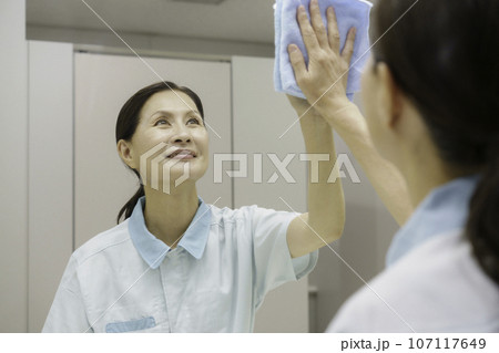 オフィスの洗面所で鏡を拭くシニア女性清掃員 107117649