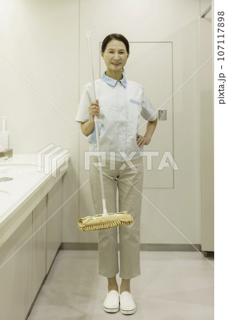オフィスの洗面所に立ってモップを持つシニア女性清掃員のポートレート　縦位置 107117898