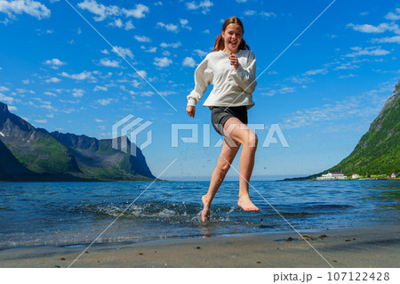 Young girl teenager running on beach in Norway Fjord. Vacation in Nordland in summer 107122428