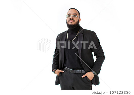 Fashion style portrait Fashionable arab business man with beard and mustache in black suit with jacket and turtleneck, wears glasses, chain, watch and belt isolate on white background Fashion style portrait Fashionable arab business man with beard and mustache in black suit with jacket and turtleneck, wears glasses, chain, watch and belt isolate on white background 107122850