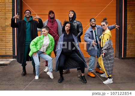 Multiracial group of young hipsters dance together on city street against orange colourful background. Diverse Stylish people outdoor, youth culture 107122854