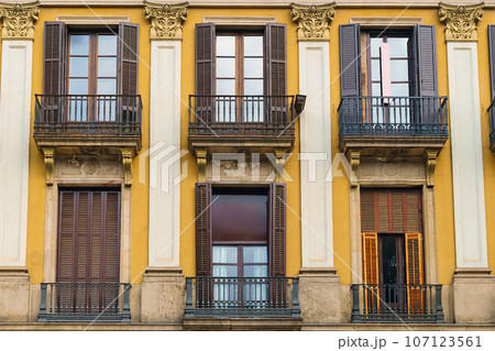 Wooden windows with shutters on yellow walls. Facade of a European antique city building. 107123561