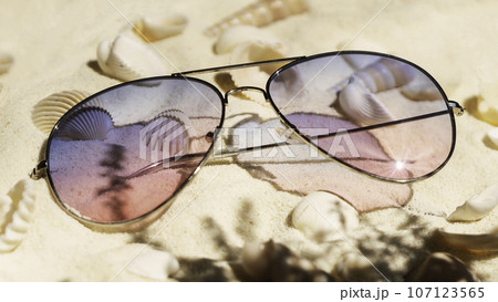 Purple and pink gradient color sunglasses on beach. Plenty of seashells on tropical sand. Purple and pink gradient color sunglasses on beach. Plenty of seashells on tropical sand. 107123565