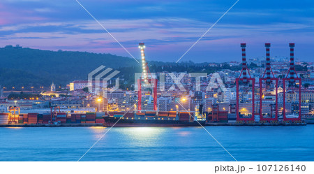 View of Lisbon port with moored sea container ship with port cranes in the evening twilight over Tagus river. Lisbon, Portugal 107126140