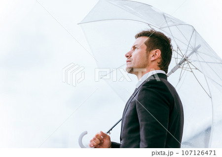 梅雨・台風の雨でビニール傘をさす外国人ビジネスマン（雨上がり・雨が止む） 107126471