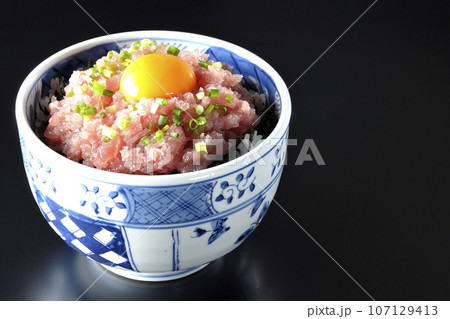 小葱と卵黄が乗っているマグロのたたき丼を黒背景で撮影 107129413