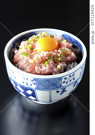 小葱と卵黄が乗っているマグロのたたき丼を黒背景で撮影 107129420