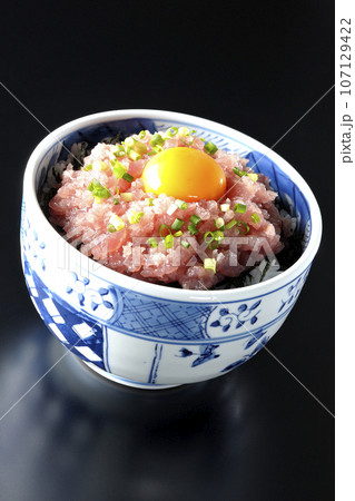 小葱と卵黄が乗っているマグロのたたき丼を黒背景で撮影 107129422