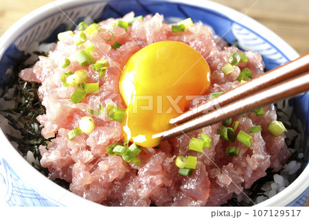 小葱と卵黄が乗っているマグロのたたき丼の卵を割る 107129517