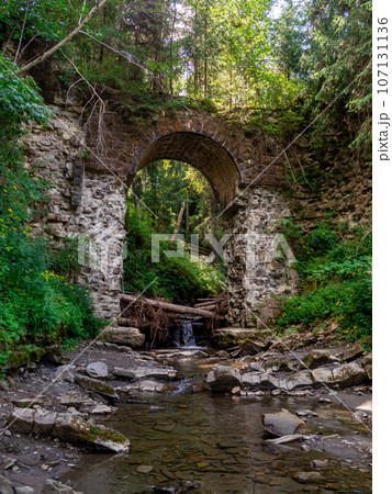 Old stone arched destroyed bridge over small river in a mountain forest Old stone arched destroyed bridge over small river in a mountain forest 107131136