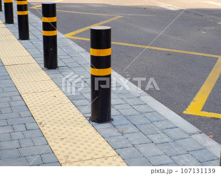 Yellow pavement for the blind on the floor on the bus stop with road bollards 107131139