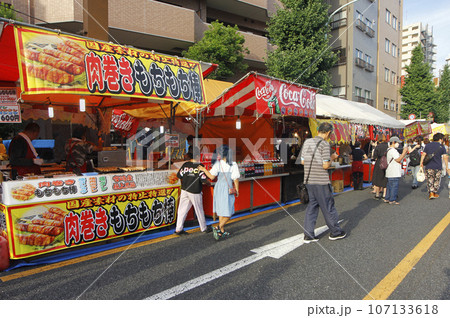 縁日の写真。露店が続く大通りはホコ天に、人々は自由気ままに散策しながら賑やかに食べ歩く 107133618
