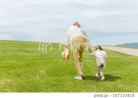 草原・公園を手を繋いで歩くママと子供の後ろ姿 草原・公園を手を繋いで歩くママと子供の後ろ姿 107133818