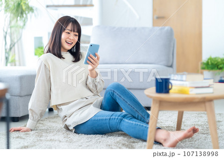 スマホを見ながらリビングでくつろぐ若い女性 スマホを見ながらリビングでくつろぐ若い女性 107138998