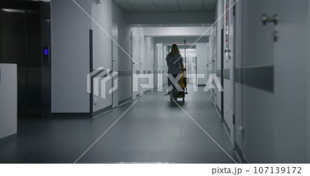 Adult nurse pushes cleaning trolley down medical center hallway Adult nurse pushes cleaning trolley down medical center hallway 107139172