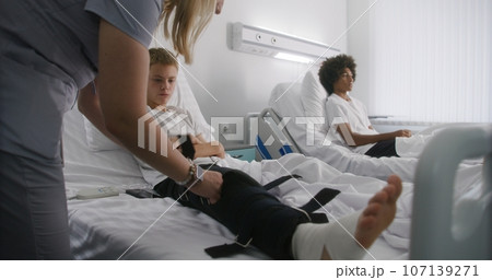 Nurse bandages leg of young boy lying on bed Nurse bandages leg of young boy lying on bed 107139271