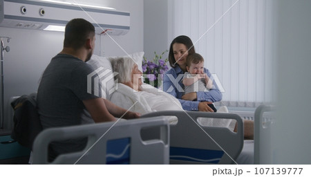 Elderly woman lies in bed in hospital ward, plays with grandson Elderly woman lies in bed in hospital ward, plays with grandson 107139777