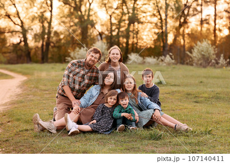 A large friendly family sits on the grass in a field in summer A large friendly family sits on the grass in a field in summer 107140411