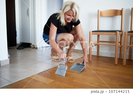 A young woman sweeps the floor of her home with a dustpan and broom. 107144215