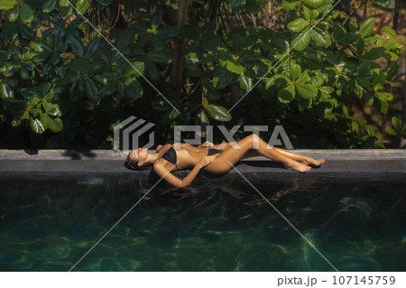 Bikini Model Relaxing in Infinity Swimming Pool at Luxury Villa Hotel in High-end Resort.  107145759