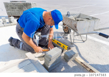 Professional bricklayer works at construction site and lays brick foundation. Man in uniform is 107147383