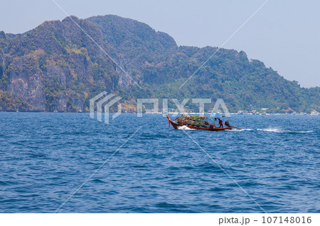Old traditional Thai motorboat made of wood for fishing and transporting tourists on excursions in the Andaman Sea in clear turquoise water under a blue sky. Travel and vacation in phuket. 107148016