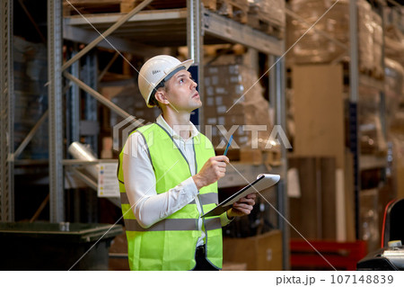 Young caucasian man worker doing stocktaking of products on shelves in warehouse 107148839