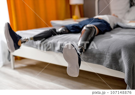 unrecognizable male lying on cozy bed in morning or after work, having bionic prosthesis 107148876