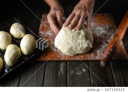 Male hands prepare dough for buns on the table close-up. Baker baking pies at home Male hands prepare dough for buns on the table close-up. Baker baking pies at home 107150325