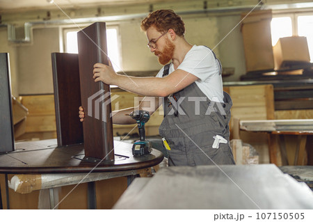 Woodworker fixing table with electric drill standing in carpentry workshop. High quality photo 107150505